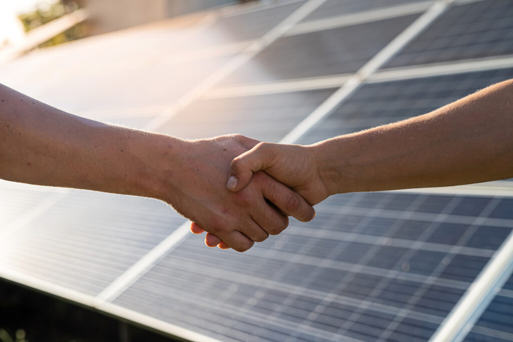 Shaking hands with solar panels in the background